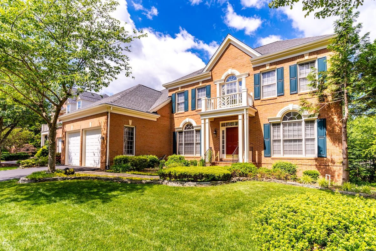 A rustic yet modern living room with a cream-colored sectional and wooden accents throughout. A large picture window shows the woods outside